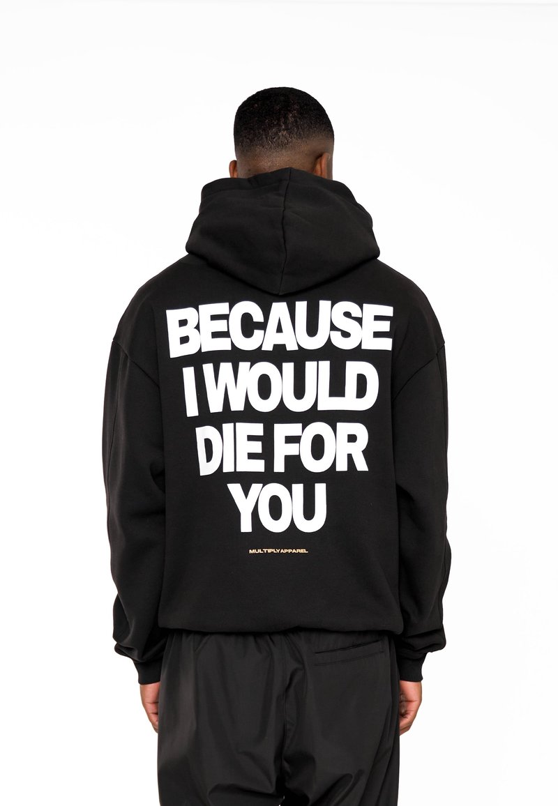 Personne portant un sweat à capuche noir avec un grand texte blanc dans le dos indiquant "Because I would die for you" et un petit texte "Multiply Apparel" en dessous.