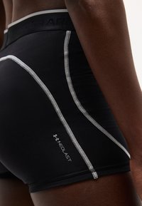 Κοντινό πλάνο ενός ατόμου που φοράει μαύρα σορτς συμπίεσης Under Armour Neolast με αντίθετες λευκές ραφές.