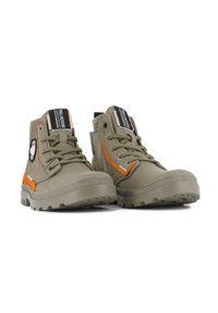Zapatillas de lona verde oliva de caña alta con acentos naranjas, suela de goma, diseño con cordones y parche de logo redondo en el costado.