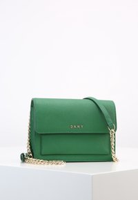Borsa a tracolla verde in pelle con catena dorata, chiusura a patta e logo DKNY inciso sul davanti. Dettagli della superficie testurizzata visibili.