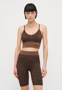Smeđa majica sportskog kroja s leopard uzorkom i odgovarajuće kratke hlače visokog struka, s rebrastim detaljima i podesivim trakama. Mekani, rastezljivi materijal.