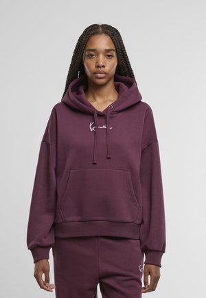 Viininpunainen huppari, jossa on etutasku, säädettävä kiristysnauhallinen huppu ja resorireunukset hihoissa. Rinnassa valkoinen kirjailtu brändäys.