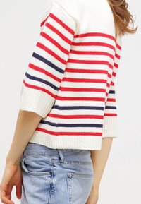 Jersey de punto a rayas en crema, con rayas horizontales rojas y azul marino, mangas cortas, textura de canalé y un diseño recortado.