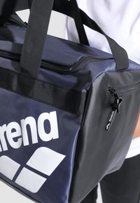 Bolsa de deporte azul y negra hecha de un tejido duradero. Presenta un gran logo blanco, cierre de cremallera y asas negras resistentes para un fácil transporte.