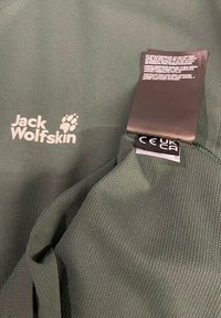 Vêtement vert Jack Wolfskin avec logo et étiquette d'entretien affichant les marques de certification CE UKCA.