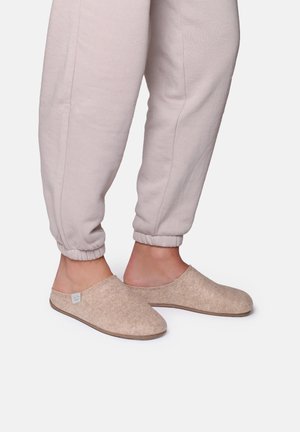 Beige felt slippers with rounded toe, open back, and flat sole, paired with light-colored sweatpants featuring elastic cuffs.