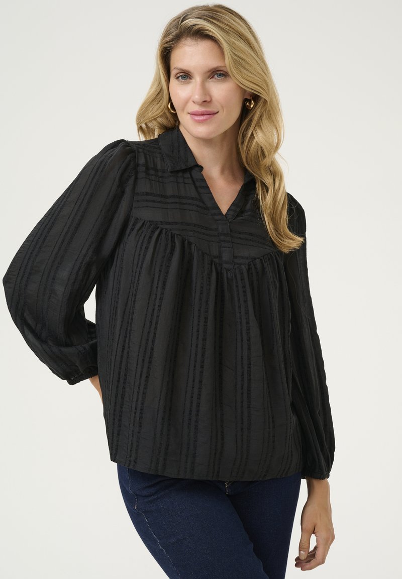 Melna blūze no teksturēta auduma ar vertikālām svītrām, ar apkakles dekoltē un apjomīgām piedurknēm.