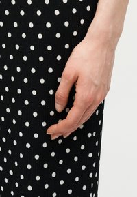 Δεξί χέρι που ακουμπάει δίπλα σε μαύρο ύφασμα με λευκές πουά, ομοιόμορφα τοποθετημένες.