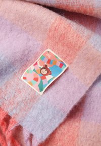 Õmmeldud ruuduline tekk pastelselt roosa, lilla ja virsiku toonides, millel on pehme tekstuur ja värviline silt karu illustratsiooniga.