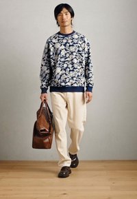 Ναυτικό μπλε φούτερ με λουλουδάτο σχέδιο, κρέμα παντελόνι, καφέ δερμάτινη τσάντα και σκούρα παπούτσια. Άνετη γραμμή με ριμπ μανσέτες και στρίφωμα.