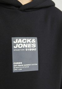 Felpa nera con cappuccio, caratterizzata da un'etichetta grigia con testo bianco, contenente il nome del marchio e le coordinate, sulla parte frontale. Tessuto in cotone con una superficie liscia.
