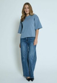 Blå bomulds oversized t-shirt med korte ærmer, parret med brede blå jeans og sorte spidse stiletter. Enkel, afslappet pasform.