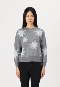 Pulover gri tricotat cu modele de stele albe, guler rotund, manșete și tiv cu țesătură la nivelul dorit, croială lejeră. Purtat cu pantaloni negri.