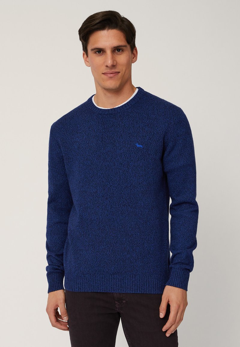 Maglione blu a maglia con un motivo texturizzato, collo a giro e polsini a coste. Presenta un piccolo logo blu sul petto. Pantaloni scuri completano l'outfit.