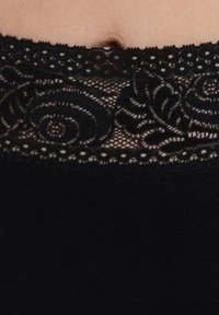 Indumento nero con una fascia in pizzo in vita, decorato con motivi floreali e bordi ondulati, che mette in risalto la texture e i dettagli intricati.
