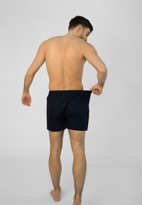 Shorts de bain pour homme couleur navy avec une taille élastique, longueur au-dessus du genou et texture de tissu lisse, vus de l'arrière.