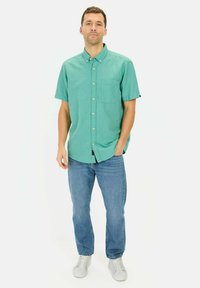 Korte mouwen, geknoopte overlshirts in teal, van een katoenmix met een borstzak, gecombineerd met blauwe denim jeans en witte sneakers.