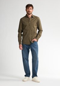 Camisa de botones verde con estampado, jeans azul claro y zapatillas blancas. La camisa tiene un cuello y una textura suave.