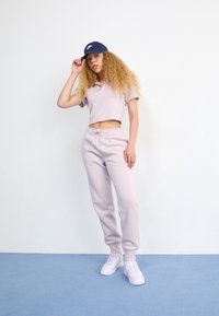 Světle fialová zkrácená polo košile s krátkým rukávem, ladící joggingové kalhoty a bílé tenisky. Námořnická kšiltovka dokončuje outfit.