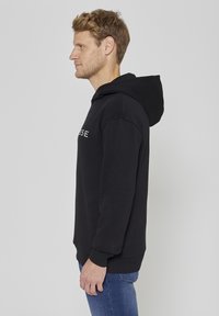 Sweat-shirt noir à capuche avec une coupe décontractée, doté de poignets et d'un ourlet côtelés. Le tissu semble doux et présente un marquage minimal à l'avant.