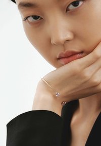 Pulsera de oro con piedras preciosas moradas, que presenta un diseño elegante y minimalista con una textura suave, llevada en una muñeca desnuda.