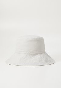 Vit bomullsbucket-hatt med en mjuk, rund krone och en bred, nedåtsluttande skärm. Har ett subtilt texturerat mönster.