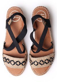 Espadrilli sandaalid, millel on pruun sisetald, mustad elastsed rihmad ja kootud jute riba musta geomeetrilise mustriga.