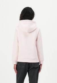 Sudadera con capucha rosa hecha de un tejido suave, con un corte holgado, puños acanalados y un bolsillo tipo canguro. Combinada con jeans oscuros.