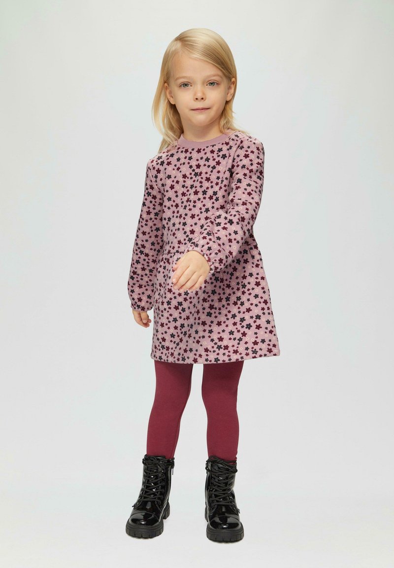 Robe rose à manches longues avec un motif floral noir, associée à des leggings bordeaux et des bottes à lacets noires brillantes. Design simple et décontracté.