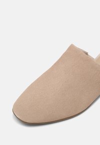 Beige mockask slip-on sko med spetsig tå och slät sula. Utsidan har en mjuk textur och sömlös design.