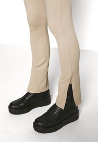Beige ribbade byxor med sidoklyftor, kombinerade med svarta platåstövlar med snörning och rundad tå. Slät textur på tyg och läder.