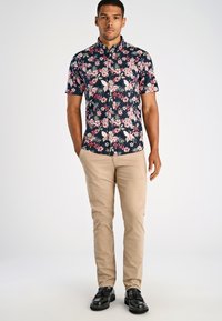 Koszula w kwiaty z krótkim rękawem ma ciemne tło z różowymi i białymi kwiatami, sparowana z beżowymi spodniami i czarnymi mokasynami.