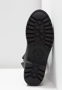 Black rubber sole with textured grip patterns, featuring a circular logo and size markings. The shoe has a rounded toe and flat design.