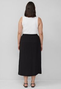 Zwarte maxi rok met een elastische tailleband, gemaakt van een textuurstof en voorzien van zijsplitsen voor meer bewegingsvrijheid, gecombineerd met een witte mouwloze top.