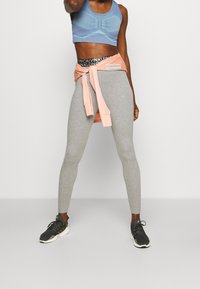Grå leggings med en tætsiddende design, parret med en lyseblå sportstop med teksturerede mønstre. En lyserød sweatshirt er bundet om livet.