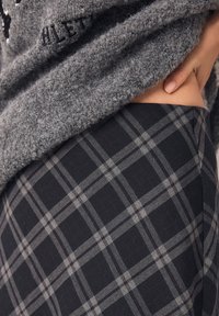Pull gris pelucheux superposé à des leggings à carreaux noirs et gris, présentant un motif texturé avec des lignes et des carrés prononcés.