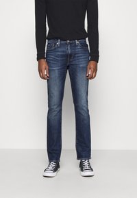 Mörkblå denimjeans med raka ben, lätt blekning och visslingar, kombinerat med en svart långärmad topp och svarta sneakers.
