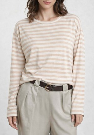 Donna che indossa una maglia a maniche lunghe beige a righe bianche infilata in pantaloni beige chiaro a vita alta con cintura marrone scuro.