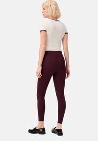 Bordeaux leggings met een hoge tailleband, gecombineerd met een wit shirt met grijze afwerking. Gladde textuur, slim fit en gepolijste zwarte schoenen.