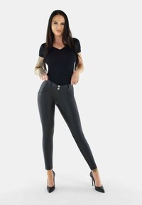 Black faux leather leggings with a high waist, front pockets, and two-button closure, paired with a fitted black V-neck top and high heels.