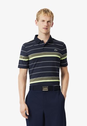 Polo shirt della marina con righe orizzontali verdi e bianche, dotato di colletto e logo Lacoste. Abbinato a pantaloni scuri e una cintura.