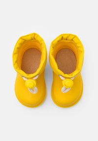 Bottes imperméables jaunes avec un extérieur lisse, une forme arrondie et un haut élastique. Elles présentent une corde décorative et un système de fermeture avec un stoppeur.