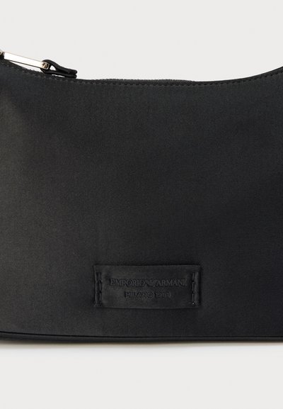Μαύρο σατέν τσαντάκι χειρός με φερμουάρ, ανάγλυφη ετικέτα λογότυπου και λεία υφή με διακριτική λάμψη. Συμπαγές ορθογώνιο σχήμα.