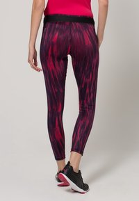 Legginsy o wysokim stanie w czarno-czerwonym abstrakcyjnym wzorze. Wykonane z elastycznego materiału, mają dopasowany krój i długość do kostek.