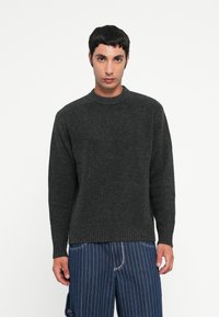 Dark gray ribbed sweater with a crew neckline, long sleeves, and loose fit. Worn over blue vertical striped pants.