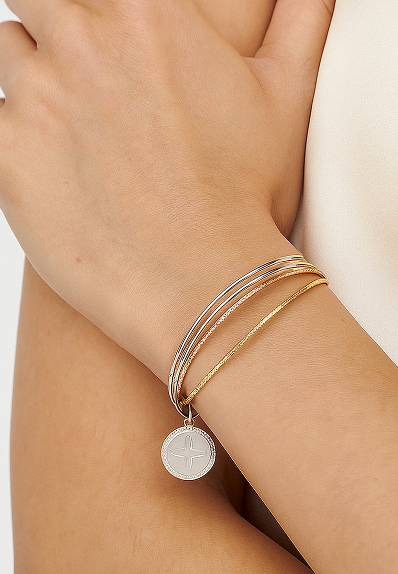 Silver and gold bracelets stacked together, featuring a textured gold strand and a circular charm with a cross design.