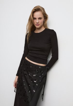 Svart långärmad topp med en figurnära design, tillsammans med en svart omlottkjol med paljetter och en texturerad, lager-på-lager look.