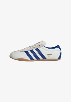 Zapatilla Adidas Tokyo blanca con rayas azules y suela de goma, diseño de corte bajo y cierre con cordones, mostrada de perfil sobre un fondo blanco.