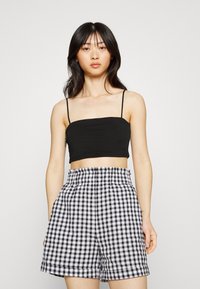 Top curto preto com alças finas, emparelhado com calções de xanfre preto e branco de cintura alta, apresentando um cós elástico.