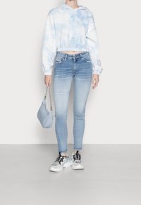 Sudadera de tie-dye azul claro, recortada y con dobladillo elástico; combinada con jeans skinny de lavado claro. Los accesorios incluyen una pequeña bolsa azul y zapatillas gruesas.